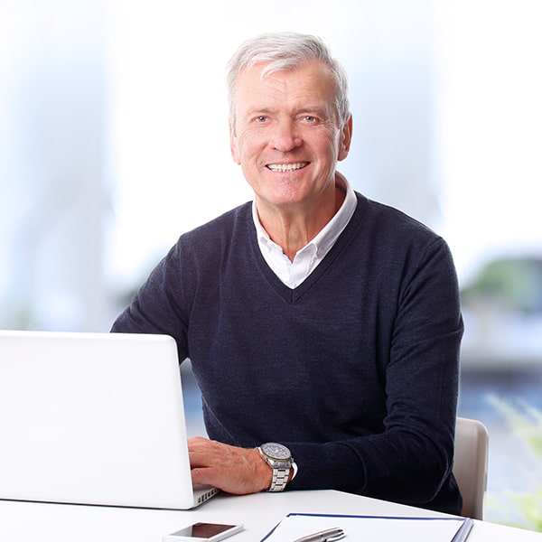 An older man smiling while using his laptop