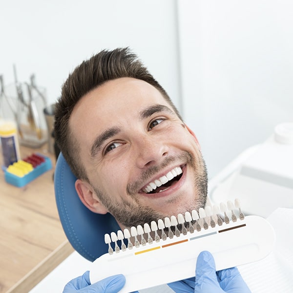 A man smiling as the dentist compares his teeth to various shades